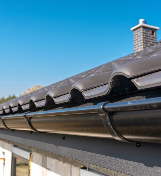 A metal, black gutter on a roof covered with ceramic tiles. Close up shot.
